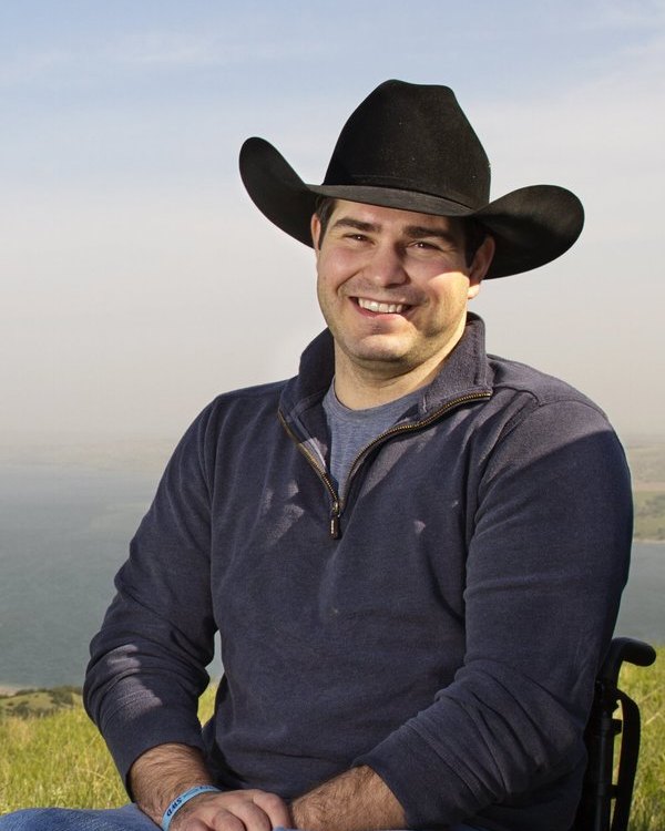Billie Sutton in a black cowboy hat, smiling on a prairie hillside