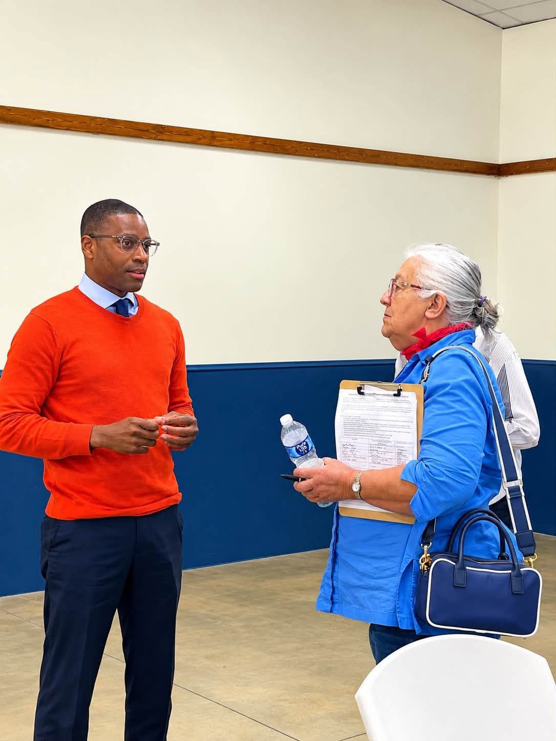 Terrence Davis in an orange sweater listening to a voter holding a clipboard